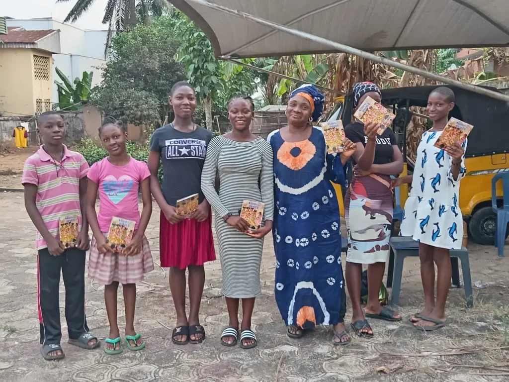 Group photo from a youth coaching and mentoring session in Africa, featuring boys and girls holding books during a morals book reading session.